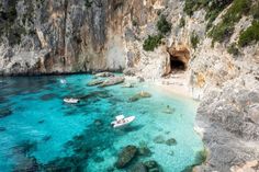 several small boats floating in the clear blue water next to a rocky cliff face and beach