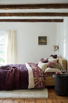 a bed sitting in a bedroom next to a window covered in purple and white blankets