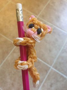 a crocheted cat on a pink stick with a pencil in it's mouth