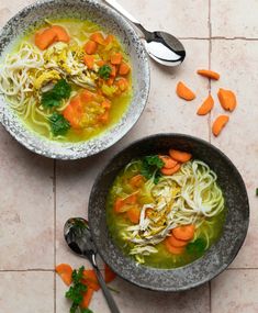 two bowls of soup with carrots and parsley on the side next to each other