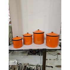 four orange canisters sitting on top of a white shelf next to other kitchen utensils