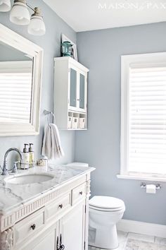 a white toilet sitting next to a sink in a bathroom under two large window shades