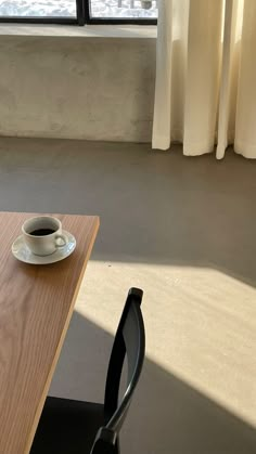 a cup of coffee sitting on top of a wooden table next to a black chair