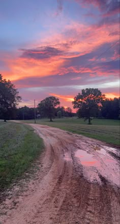 a dirt road that has some water on it and trees in the background at sunset