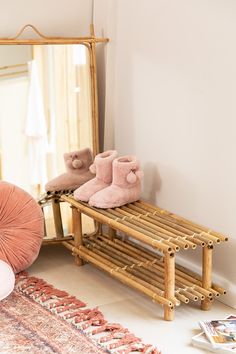 there is a bamboo shoe rack in the corner with pink slippers next to it