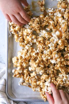 two hands reaching for caramel popcorn on a baking sheet