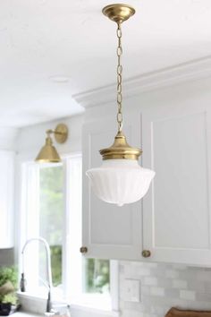 a kitchen with white cabinets, gold fixtures and a light fixture hanging from the ceiling