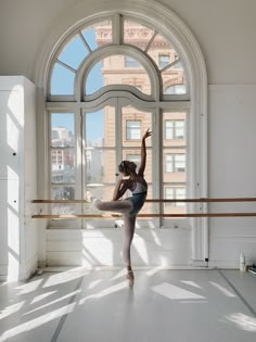 a young ballerina is practicing her moves in front of a large window with arched windows