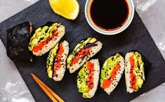 sushi with sauce and chopsticks on a slate board next to a cup of tea