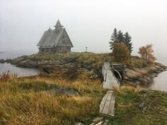 a wooden walkway going up to a house on an island in the middle of water