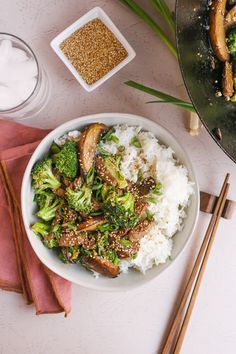 a bowl filled with rice and broccoli next to chopsticks on a table