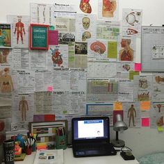 a laptop computer sitting on top of a desk next to a wall covered in papers