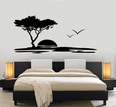 a bed sitting under a tree next to a wall with birds flying over it in front of a sunset