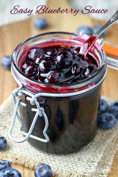 a glass jar filled with blueberry jam on top of a table next to fresh blueberries