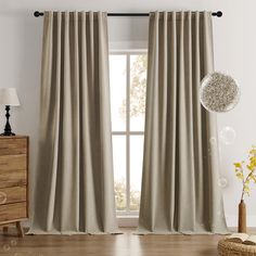 a living room with white walls and wooden flooring, two windows covered in beige curtains