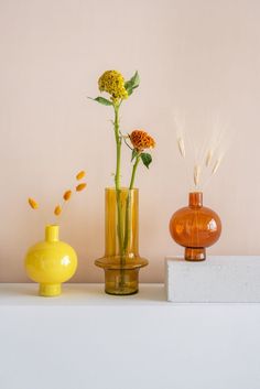 three vases with flowers in them sitting on a white shelf next to each other