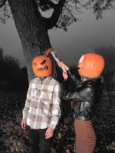 two people wearing pumpkin heads standing in front of a tree with their hands on each other's head