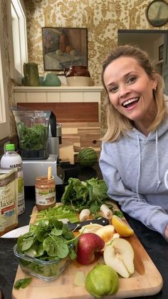 a woman sitting in front of a cutting board filled with fruits and vegetables