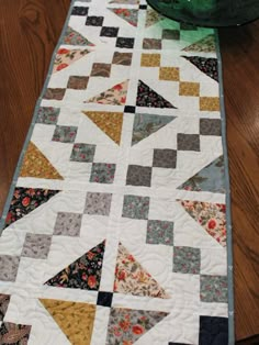 a quilted table runner on top of a wooden floor next to a green vase