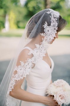 a woman in a wedding dress holding a bouquet and wearing a veil with flowers on it