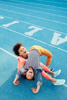 two children are playing on the blue running track with their hands in each other's pockets