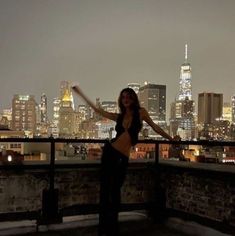 a woman standing on top of a roof in front of a city skyline at night