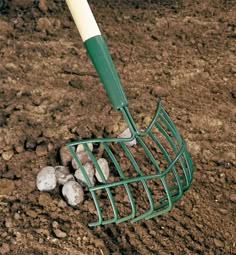 a green and white rake sitting on top of dirt covered ground next to some rocks