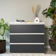 a white and black dresser next to potted plants