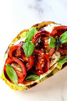 an open faced sandwich with tomatoes, lettuce and sauce on it sitting on a marble surface