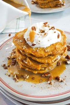 a stack of pancakes with whipped cream and pecans on top, being drizzled with syrup