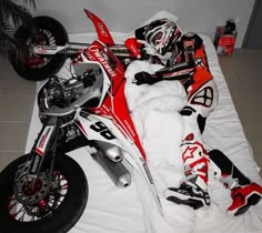 a red and white dirt bike laying on top of a bed next to a motorcycle