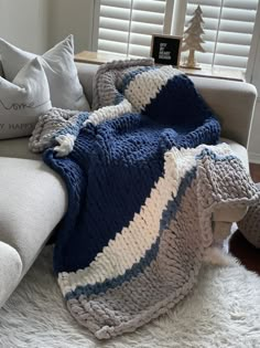 a white couch with a blue and gray blanket on it's back next to pillows