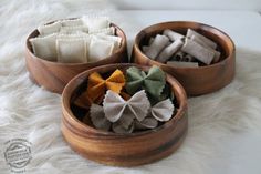 three wooden bowls filled with different types of felt flowers on a white furnishing