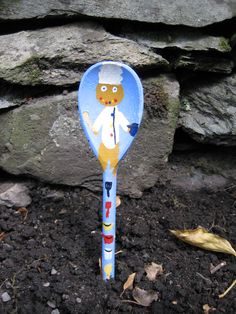 a blue and yellow spoon with a cartoon character on it sitting in dirt next to a stone wall