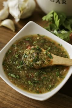 a white bowl filled with soup next to garlic and parsley on a wooden table