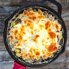 a skillet filled with cheese and vegetables on top of a wooden table