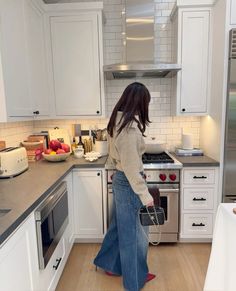 a woman is standing in the kitchen with her back to the camera and holding a purse