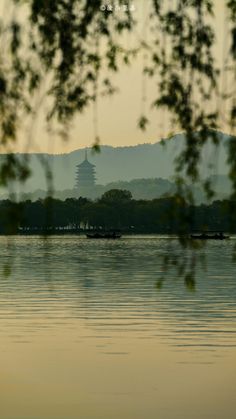 a lake with boats floating on it and a pagoda in the distance, seen from across the water