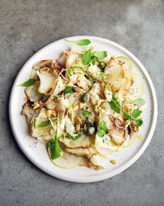 a white plate topped with food on top of a cement floor covered in green leaves