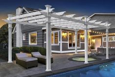 an outdoor living area next to a swimming pool at night with lights on the pergoline