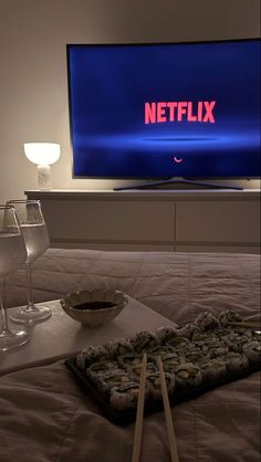 a flat screen tv sitting on top of a bed next to two glasses of wine