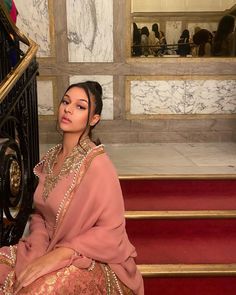 Brown girl wearing a pink desi outfit fit on grande stairs