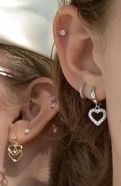 a close up of a person wearing ear rings and earrings with heart shaped charms on them