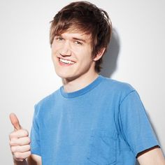 a young man is giving the thumbs up sign with his right hand while wearing a blue t - shirt