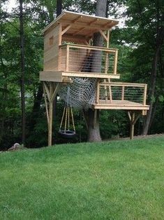 a tree house built into the side of a hill in front of trees and grass