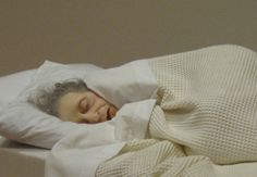 an older woman is sleeping in bed with her eyes closed and she's covered by a blanket