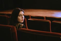 a woman sitting in an empty theater seat looking off into the distance with her eyes closed