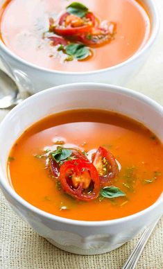 two white bowls filled with tomato soup and garnished with basil