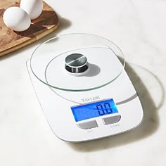 an electronic scale sitting on top of a counter next to eggs and a cutting board