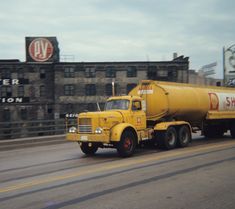 a yellow tanker truck driving down the road in front of a large building with a sign on it's side